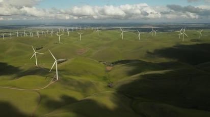 Windmills in a grassy field, as far as the eye can see. Blue sky with large, puffy grey clouds.